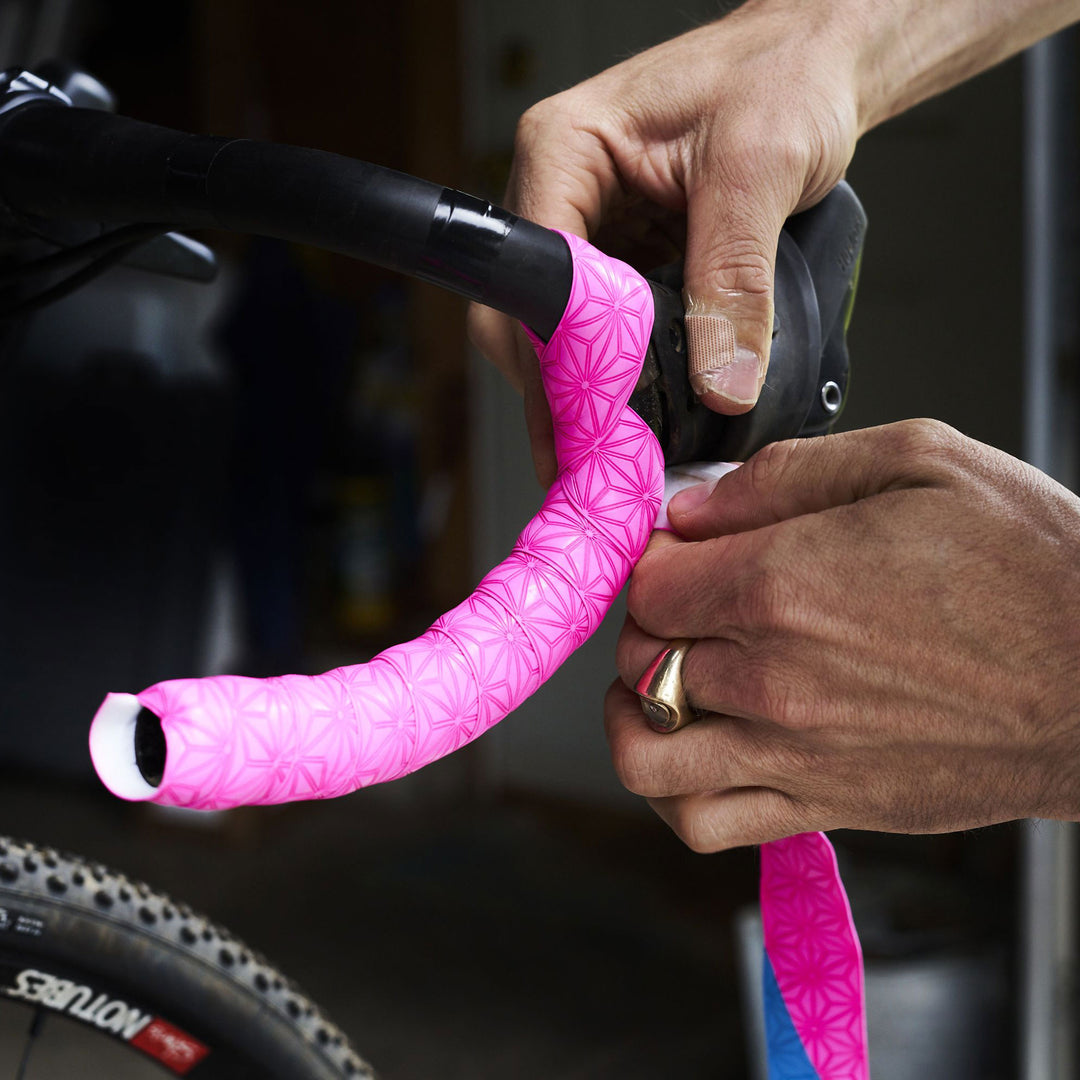A man is wrapping his bicycle handlebar with pink bar tape.